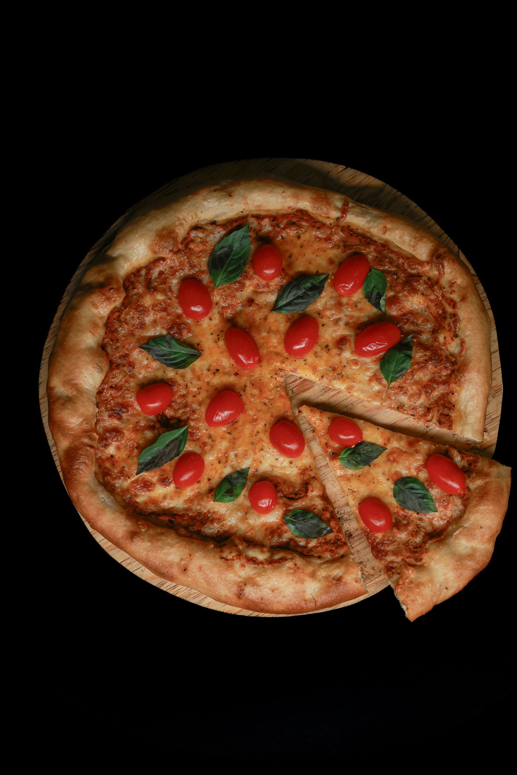Pizza tradicional com tomate cereja e manjericão sobre fundo escuro
