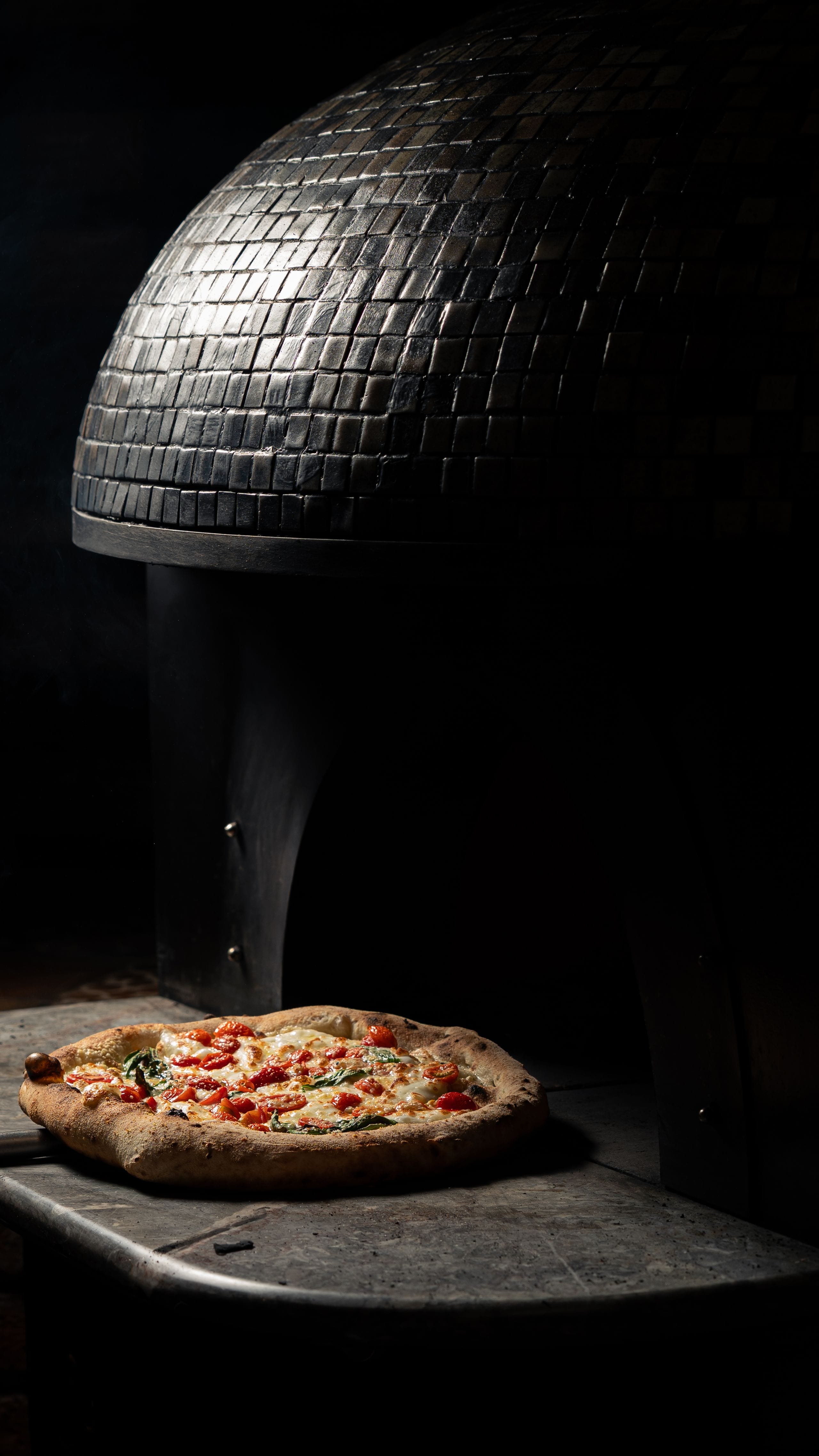 Pizza recém-saída do forno a lenha, com luz quente e fundo escuro