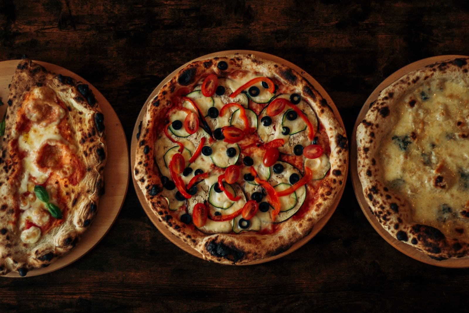 Três pizzas artesanais em mesa de madeira escura