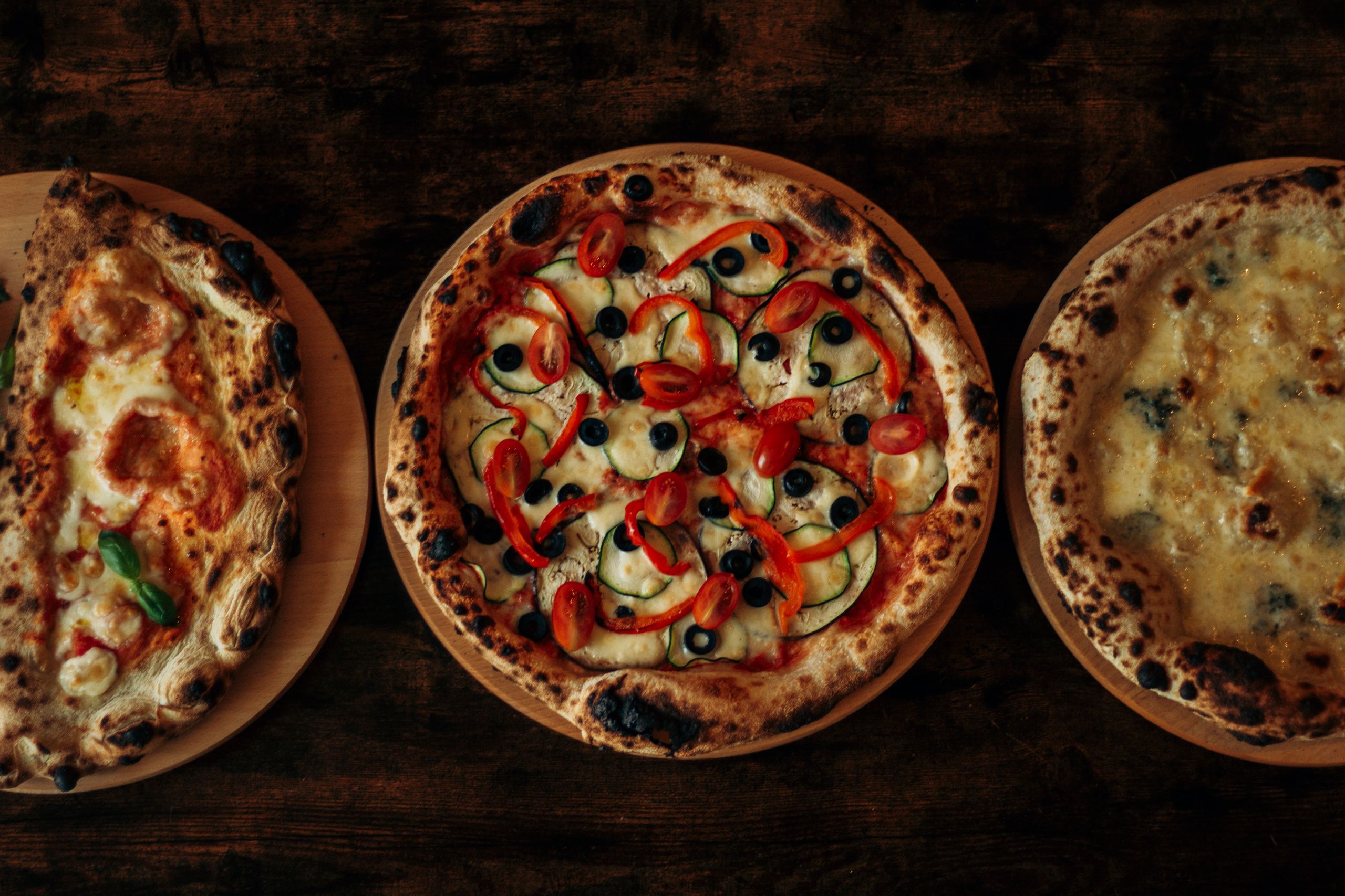 Pizzas artesanais recém-saídas do forno sobre mesa de madeira escura, com luz quente